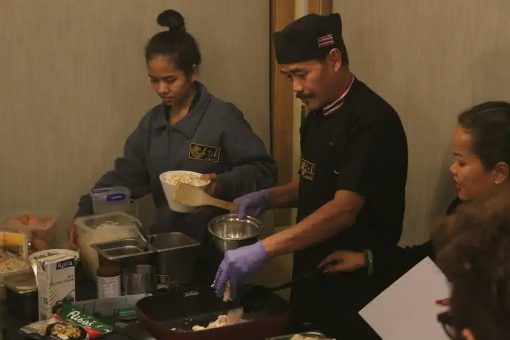 Two chefs preparing Thai food in a kitchen, cooking ingredients in a pan