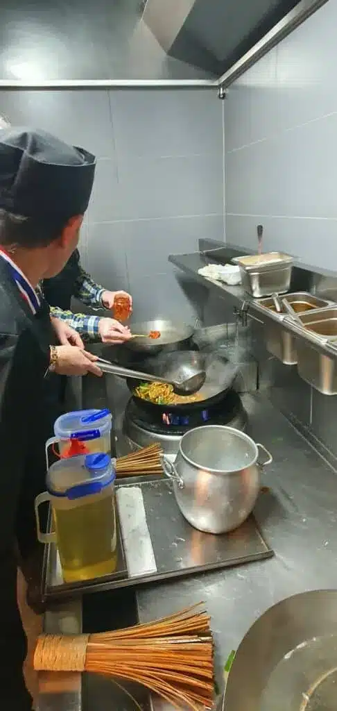 Chef cooking noodles in a wok over a gas stove