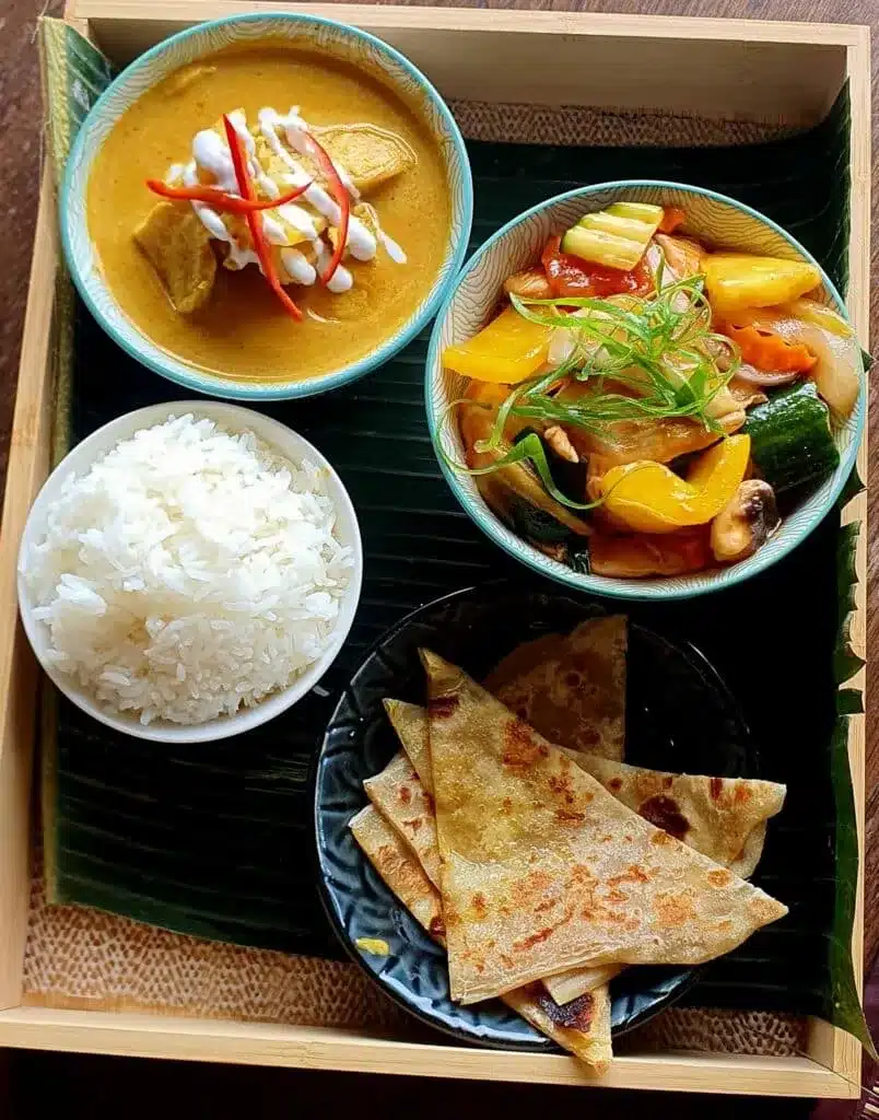 Thai meal set with curry, stir-fried vegetables, rice, and roti bread on a tray